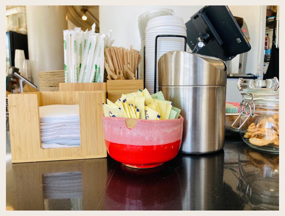 A counter detail at Highlight Coffee — sugars, spoons, and house napkins arranged in marble and stainless trays.