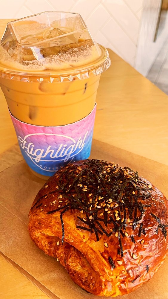 An iced butterscotch latte in a Highlight branded cup beside a kimchi spam croissant.